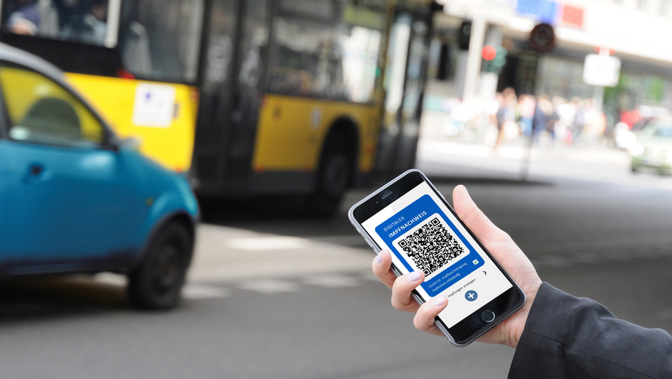 Une main devant un bus tient un smartphone avec un certificat de vaccination sur l'écran.