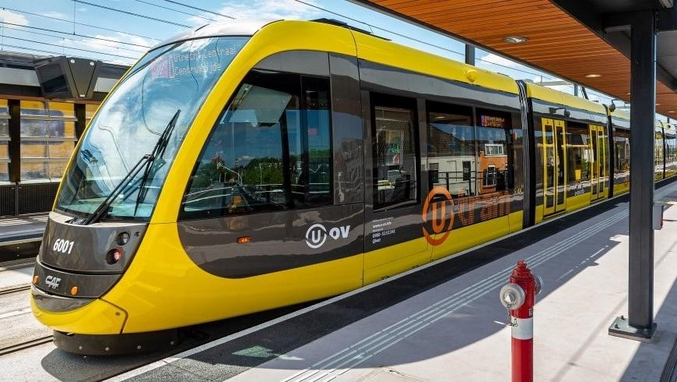 Un tramway jaune et noir de la province d'Utrecht se trouve à une station.