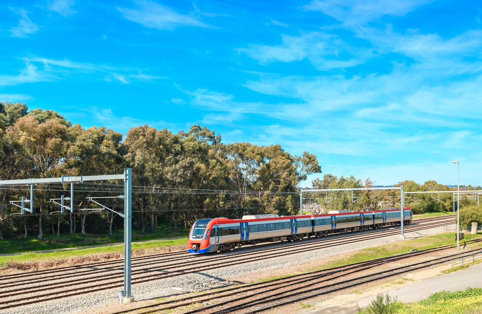 Un train Keolis rouge et argent passe de droite à gauche devant des arbres et un ciel d'un bleu éclatant.