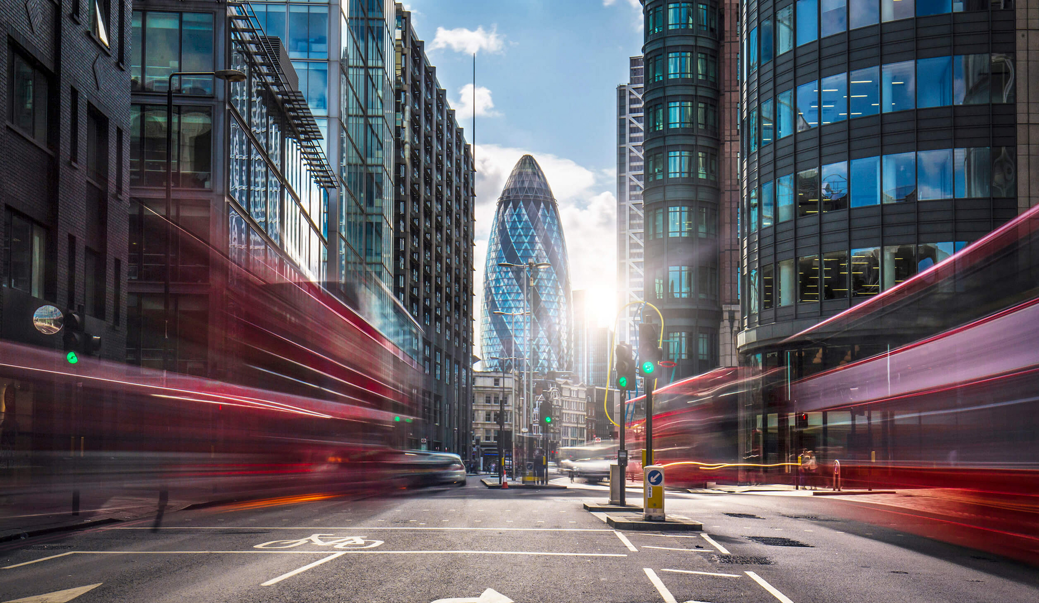 Vue du Gherkin à Londres à travers deux maisons et des bus passant à proximité, avec flou de bougé