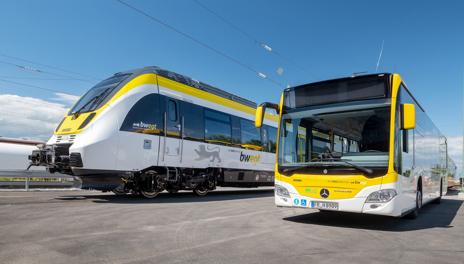 Un bus jaune et blanc vide ainsi qu'un train jaune et blanc de la SWEG se trouvent côte à côte dans un dépôt.