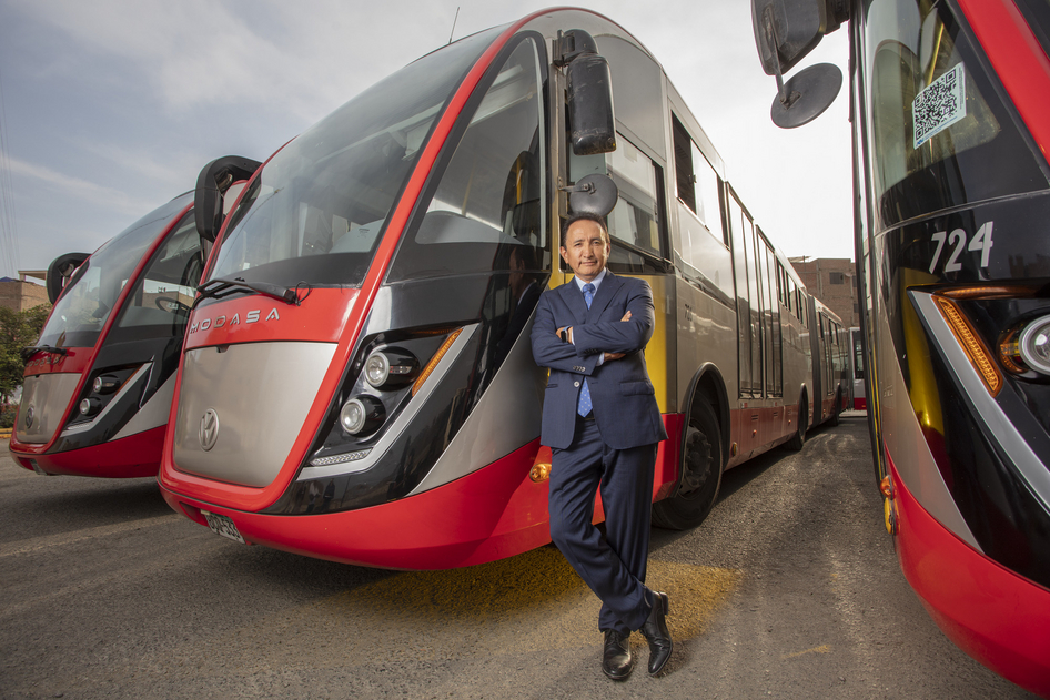 Polo Peréz, PDG du Grupo Polo, s'appuie sur un bus rouge du Grupo Polo stationné à côté de deux autres bus rouges dans un dépôt.