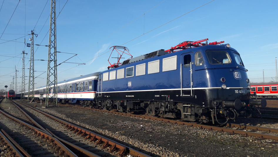 Un train bleu de TRI circule de gauche à droite sur des rails bruns.