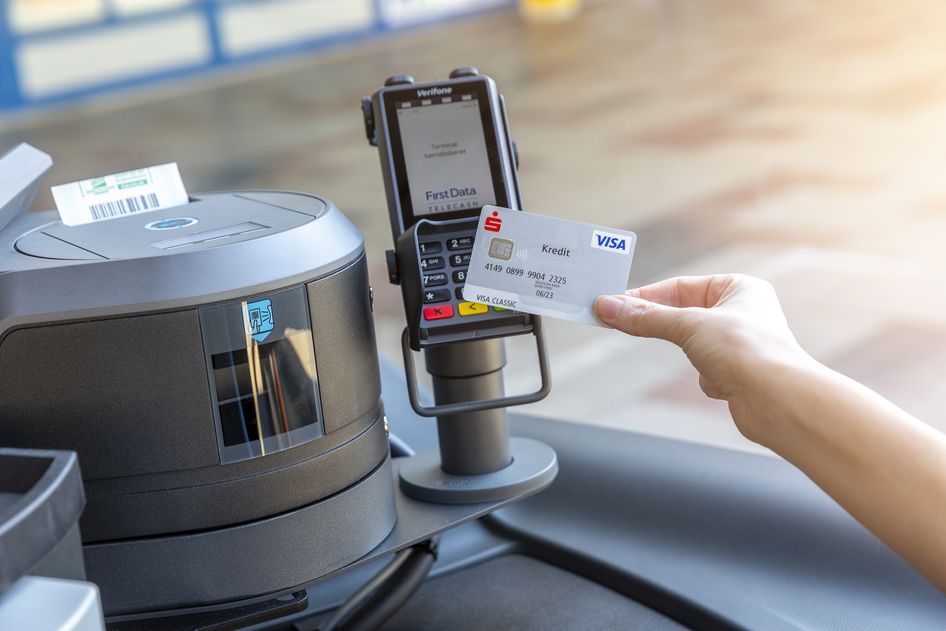 Une main tient une carte bancaire devant un terminal de paiement dans le bus pour payer le ticket sans argent liquide.