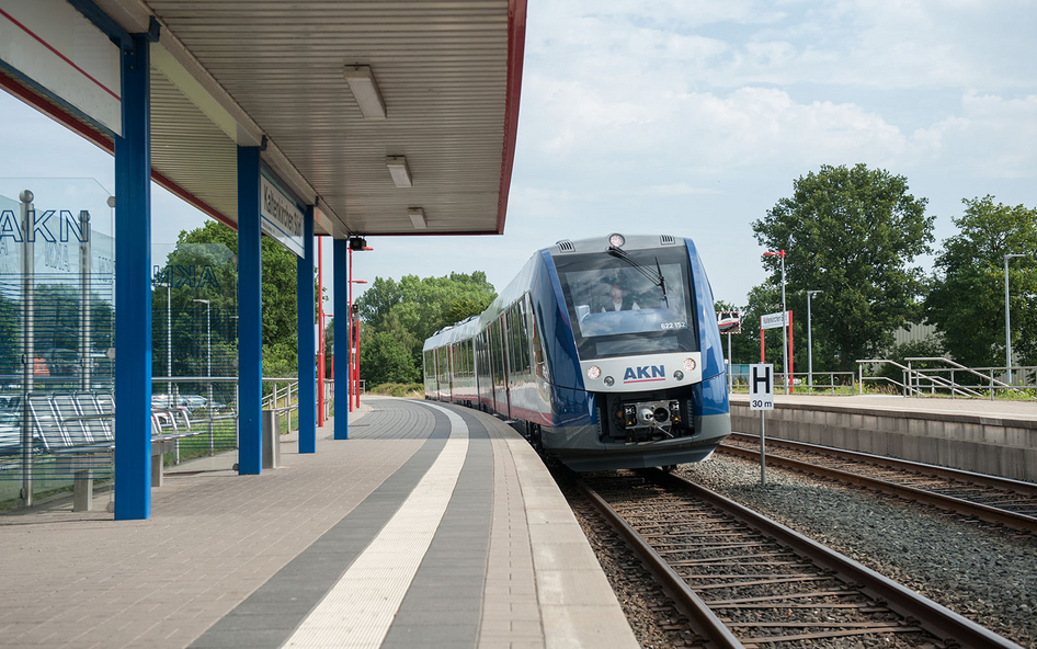 Eine blaue AKN Eisenbahn fährt fährt in einen leeren Bahnhof ein.