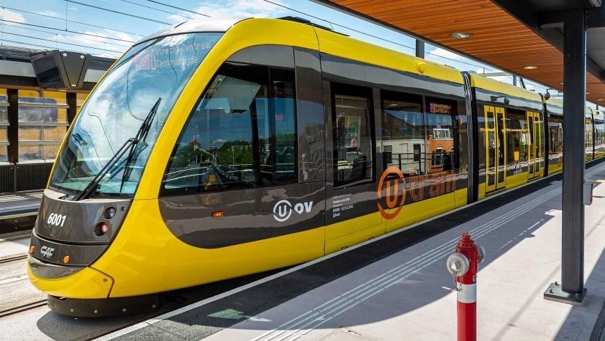 Un tramway jaune et noir de la province d'Utrecht se trouve à une station.